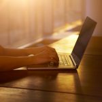 Woman typing as the sun sets behind her.