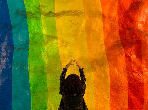 Rear View Of Woman Making Heart Shape While Standing Against Multi Colored Wall