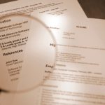 sepia toned selective focus shot of resume and magnifying glassPlease Note: All information on resume is fake